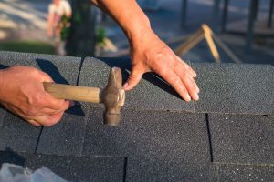 Workers hands installing bitumen roof shingles using hammer